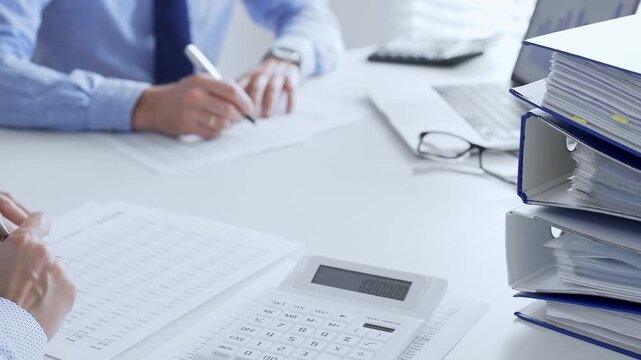Accountants collaborating on financial reports and strategies while calculating and verifying documents in an office setting. Audit and taxes in business