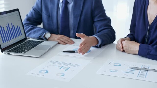 Business partners are discussing company performance and making plans based on charts and graphs displayed on laptop and printed documents. Business people and finance concept