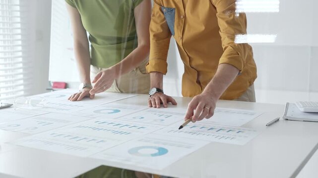 Business professionals analyzing financial reports, pointing at charts during collaborative meeting, discussing data with focused professional demeanor