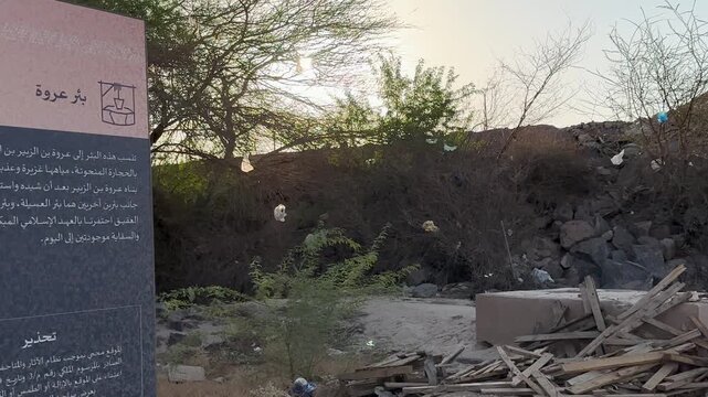 Historical Bir Urwah well sign in Medina amidst rocky terrain and debris.