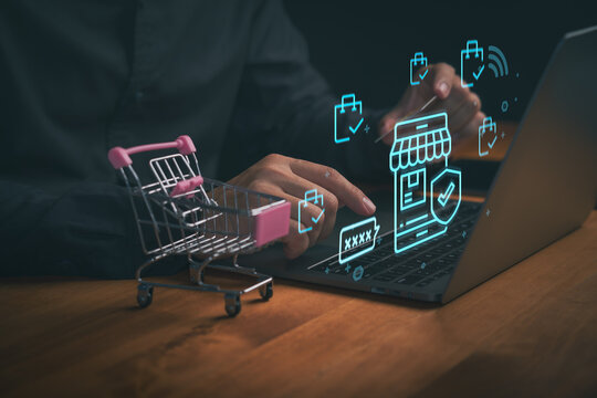 Man using laptop for online shopping with mini shopping cart. Glowing virtual store and secure payment icons. Digital marketing technology for e-commerce, internet business, cyber security and retail.