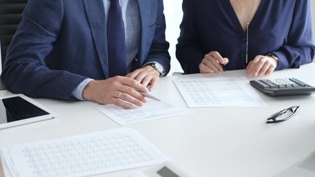 Business colleagues are reviewing financial reports and using a calculator during a productive meeting in a brightly lit office setting. Audit and taxes in business