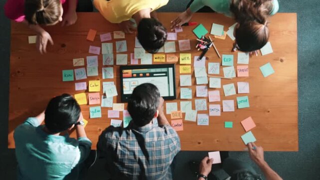 Top down view of programmer brainstorming and planning about web design while looking at tablet wireframe prototype. Aerial view of skilled developer team talking about digital application. Symposium.