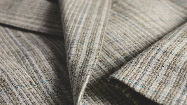 A close-up of a grey wool suit jacket highlights textured striped tweed fabric, menswear patterns, lapels, clean stitching, three cuff horn buttons, blue threads, tailoring, and craftsmanship.
