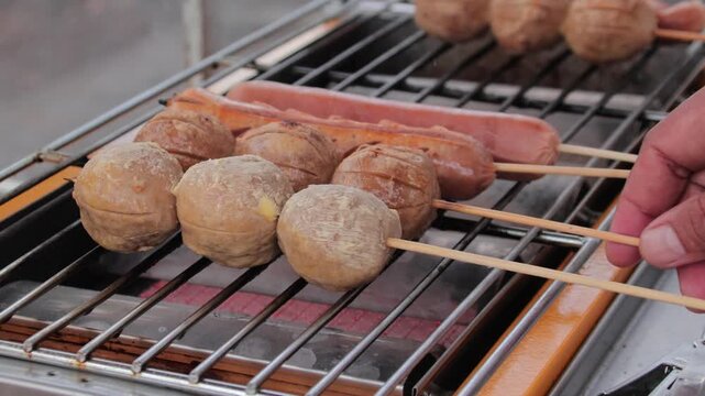 Grilled meatballs and sausages on skewers being cooked on a grill