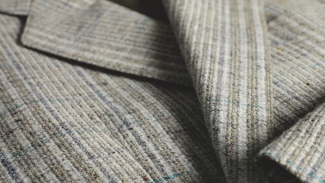 A close-up of a grey wool suit jacket highlights textured striped tweed fabric, menswear patterns, lapels, clean stitching, three cuff horn buttons, blue threads, tailoring, and craftsmanship.