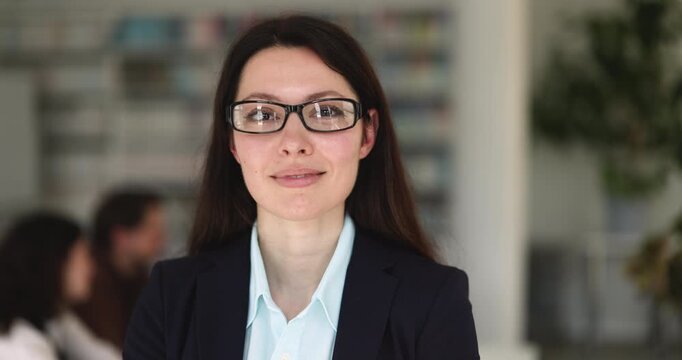 Headshot portrait adult female business or academic professional in formal suit and glasses looking at camera in office or library presenting herself with confident smile for authority and expertise