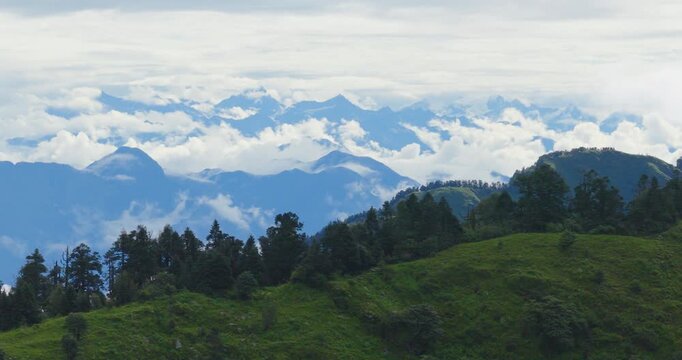 Aerial shot of Badimalika, Bajura, Nepal, of a lush green tree-lined mountain ridge with a thick cloud sea floating over distant mountain ranges under a soft clouded sky