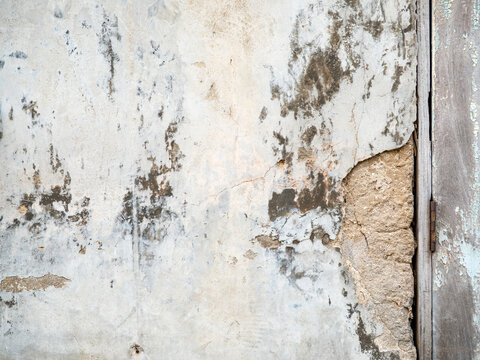 Weathered white plaster wall with cracked peeling stucco and exposed cement, rusty door hinge and old wooden door, grunge shabby texture background with copy space