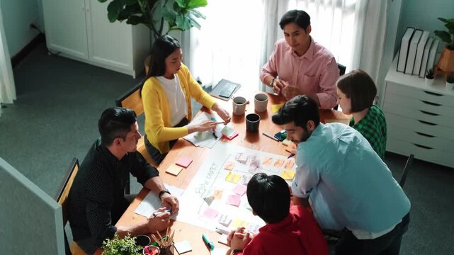 Top down view of diverse people brainstorming and making scrum task board. Group of skilled business team working together and using kanban board while shake hands for making agreement. Convocation.