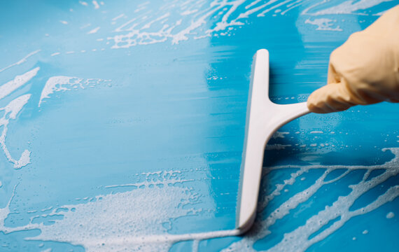 Gloved hand clearing foam from a blue surface with a squeegee leaving a broad strip.