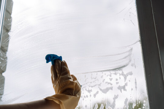 Gloved hand wiping the lower window with a blue cloth through curved foam streaks.