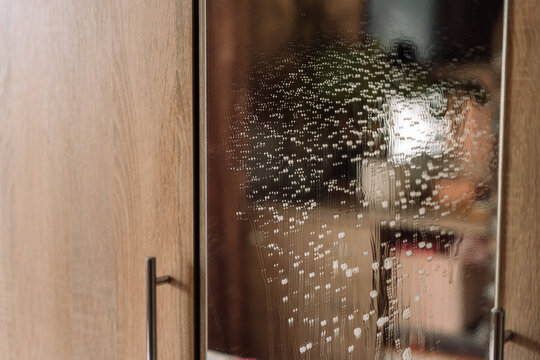 Cluster of cleaning foam dripping down a wardrobe mirror with blurred reflections.