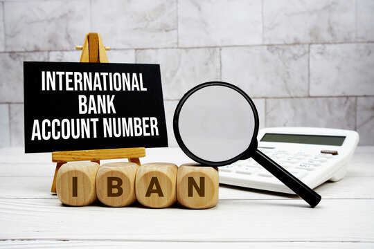 IBAN International Bank Account Number text with calculator magnifying glass and on wooden background