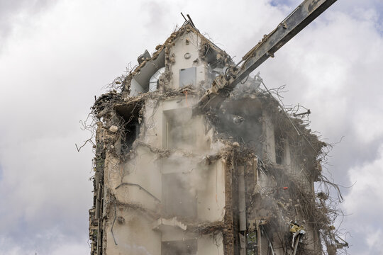 Close-up of a heavy excavator arm breaking down the walls and floors of a tall residential building during urban demolition.