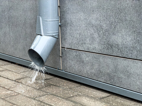 flow of rainwater pouring from a metal downspout during a heavy rain.