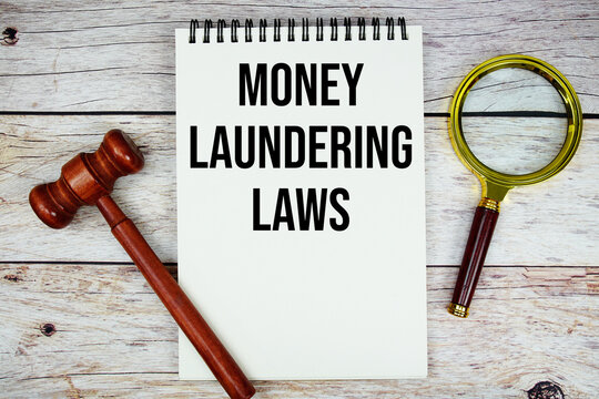 Money Laundering Laws text written on notepad with wooden judgment gavel and magnifying glass on wooden background