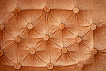 Close-up of warm brown velvet upholstery with deep button tufting, creating a luxurious soft textile texture and geometric pattern for furniture, interior design and elegant backgrounds. © Marek