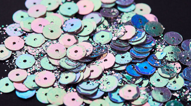 Holographic iridescent sequins and glitter macro texture on black background. Close-up of metallic pink, teal, and blue sparkling spangles for festive fashion design.