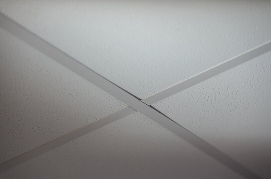 Close-up of a clean white suspended acoustic tile ceiling with metal grid, showing modular drop ceiling construction, geometric pattern and modern commercial interior finishing.