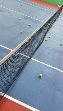 Indoor tennis court photographed from behind the baseline with tennis balls visible ahead, emphasizing depth and the structured playing environment