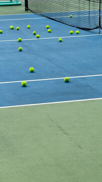 Tennis balls beside the baseline of an outdoor court in early morning light, capturing the quiet atmosphere before a match or training session