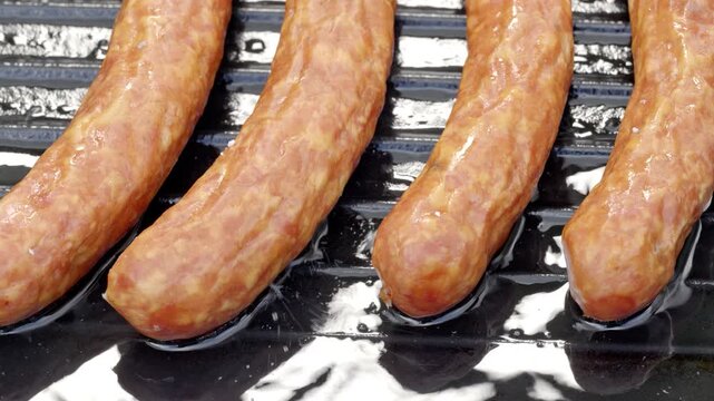 Raw sausage links resting on dark grill grates, glossy marbling and bright reflections, side by side in top view food prep with bright light