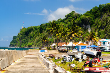 Obraz premium View of the fishing port area with boats, palm trees, and lush green cliffs in Grand Riviere, Martinique.