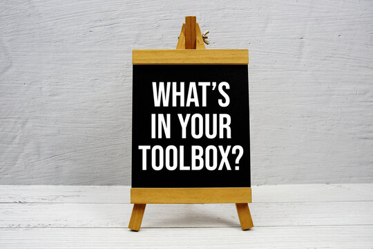 What's In Your Toolbox? text written on wooden easel stanind on wooden background
