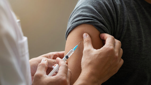 Doctor administering vaccine injection into arm of male patient.