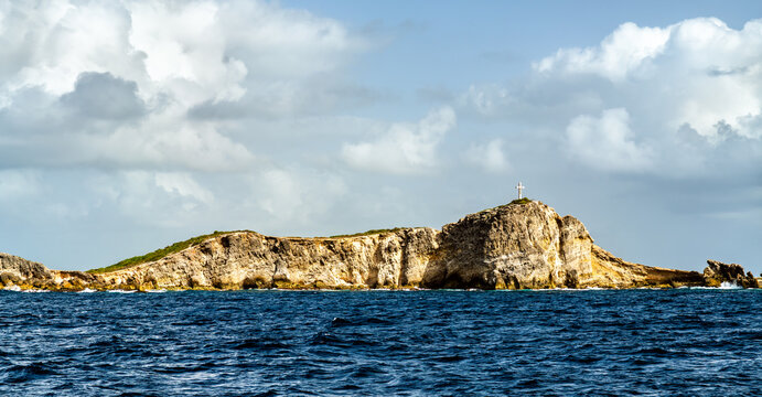 Panoramic view of the rocky peninsula of Pointe des Chateaux and its landmark cross surrounded by the blue sea under a cloudy sky in Guadeloupe, Caribbean France