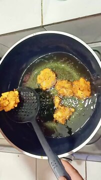 Deep frying golden food pieces in hot oil with spatula flipping with set against bright indoor kitchen backdrop transferring them strainer draining