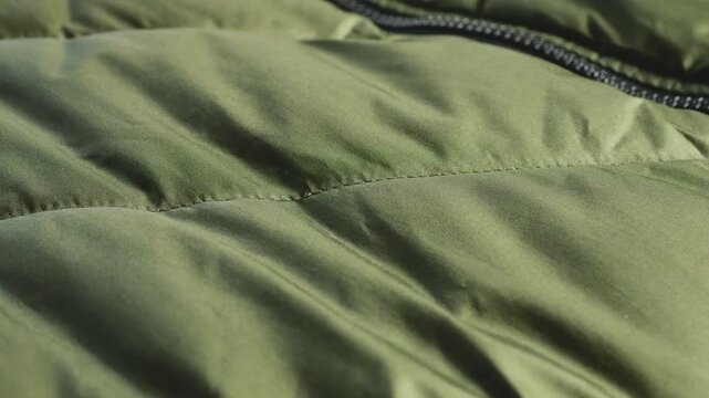 Close-up of a green quilted jacket fabric. Close up shot of olive green jacket pocket zipper. Detail of textile windproof casual apparel. Outerwear element texture on clothing material.