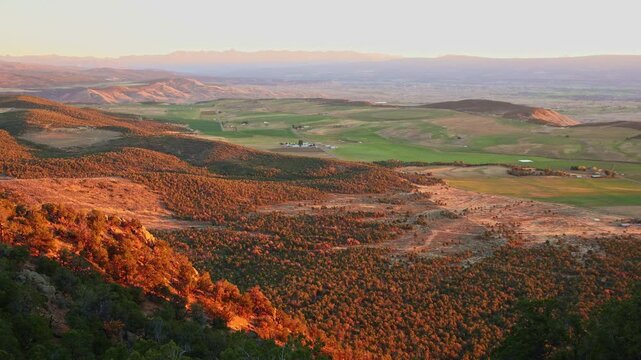 Warm evening sunlight illuminates lush farmland valleys and distant mountain ranges from Warner Point trail in Colorado