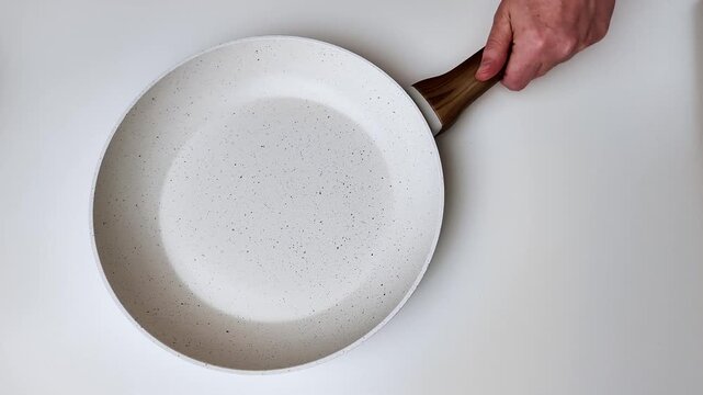 A person holds a white speckled frying pan with a wooden handle, shown in a sequence of three vertical frames against a plain light gray background