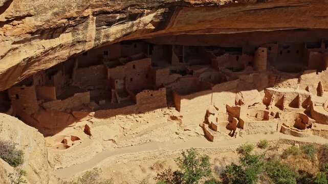 Warm sunset light illuminates ancient masonry dwellings nestled beneath towering sandstone cliffs at Mesa Verde Cliff Palace