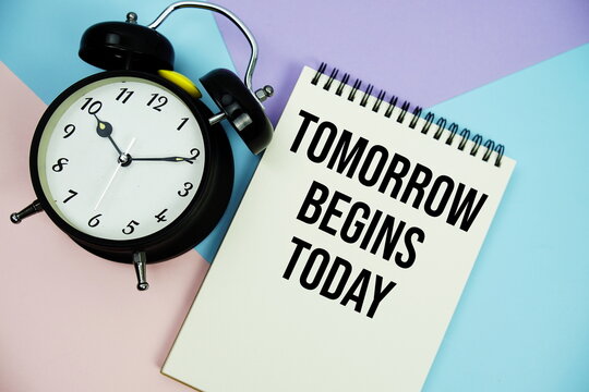 Tomorrow Begins Today text written on notepad with alarm clock flat lay on multicolor pastel background