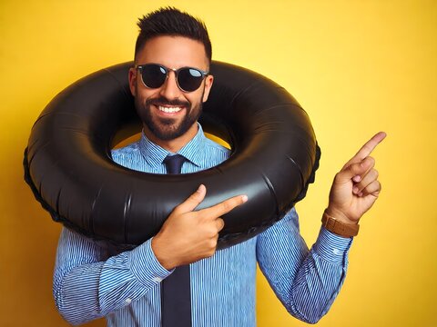 Cheerful smiling young businessman wearing black swim ring and sunglasses pointing his finger towards empty copy space on yellow background.