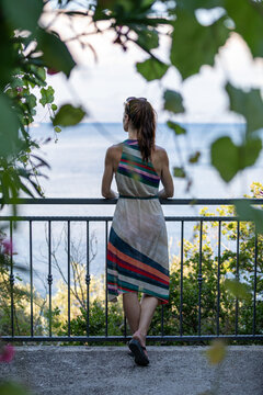 A brunette woman stands alone, leaning against a fence and lost in thought. The quiet setting and her contemplative pose create a peaceful, reflective atmosphere.