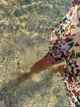 A woman in a light summer dress with a delicate butterfly pattern walks through the sea, enjoying the warm water and peaceful summer surroundings.