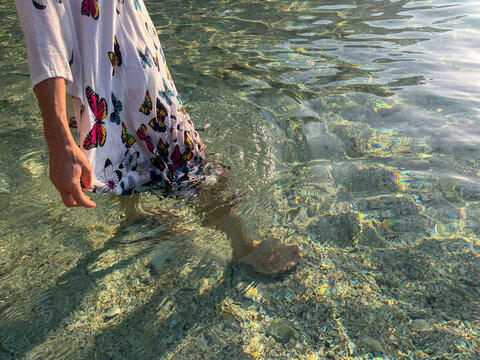 A woman in a light summer dress with a delicate butterfly pattern walks through the sea, enjoying herself in the warm summer day and the peaceful surroundings.