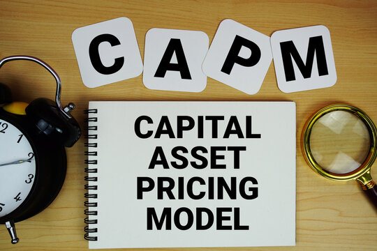 CAPM Capital Asset Pricing Model text written on notepad with magnifying glass and alarm clock on wooden background