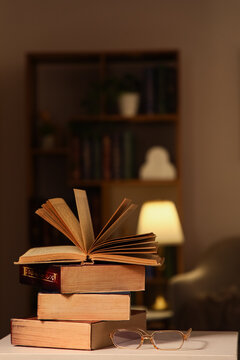 Education and lifelong learning, open book on a stack of vintage books with reading glasses in a cozy library room with warm lamp light at night