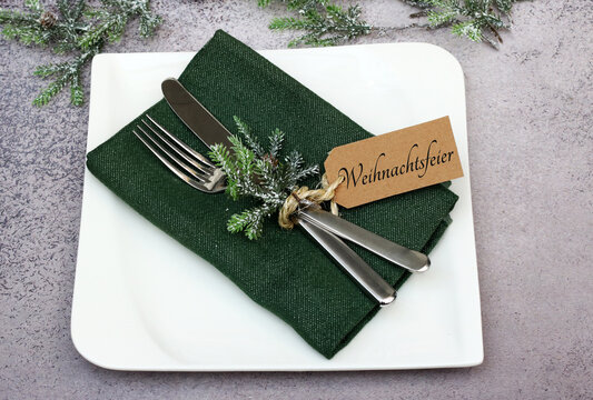 Festliche Tischdekoration zur Weihnachtsfeier mit gr&uuml;ner Stoffserviette, Besteck, Tannenzweig  und weissem Teller.