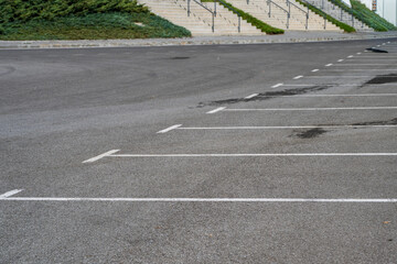 Obraz premium An empty outdoor asphalt parking lot is marked with white painted parking bays in front of landscaped hills and tiered concrete staircases