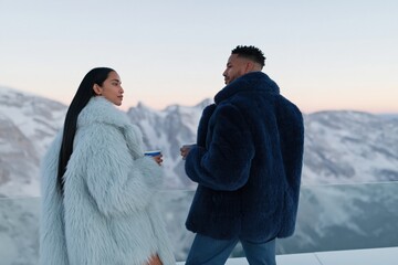 Obraz premium Two people in pastel and navy fur coats holding cups on glass terrace for winter fashion lifestyle banner and travel background
