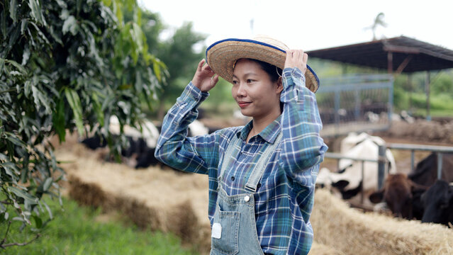 Portrait of Asian female farmer wearing straw cowboy hat standing in front of cow pen on rural livestock farm.