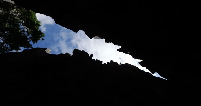 Nadir-angle spinning shot looking upward through narrow, jagged crevice at Shilin Stone Forest in Yunnan, China. High-contrast silhouettes of towering limestone walls frame diagonal sliver of blue sky