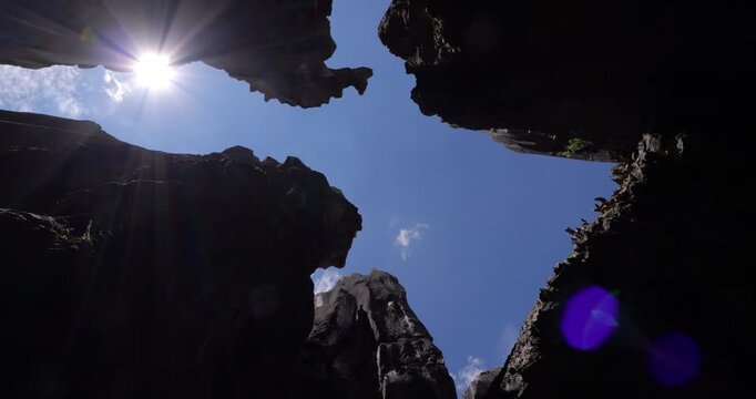 Spinning, extreme low-angle view captures dramatic silhouetted karst formations at Shilin Stone Forest in Yunnan. Sharp limestone rocks rise high, framing blue sky with vibrant sun star