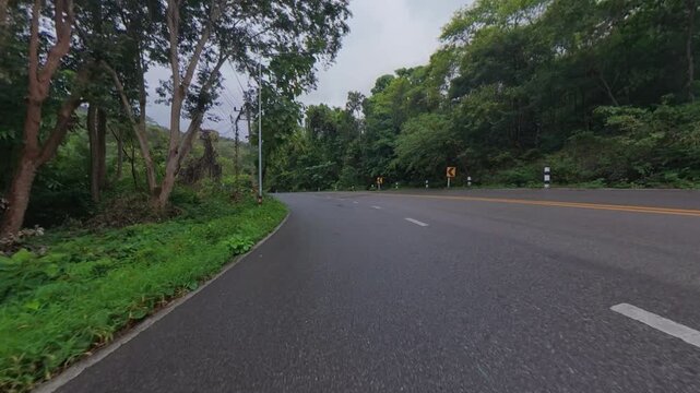 Scenic winding road through lush green forest, featuring road curves, roadside vegetation and a peaceful tropical landscape suitable for travel and transportation concepts.